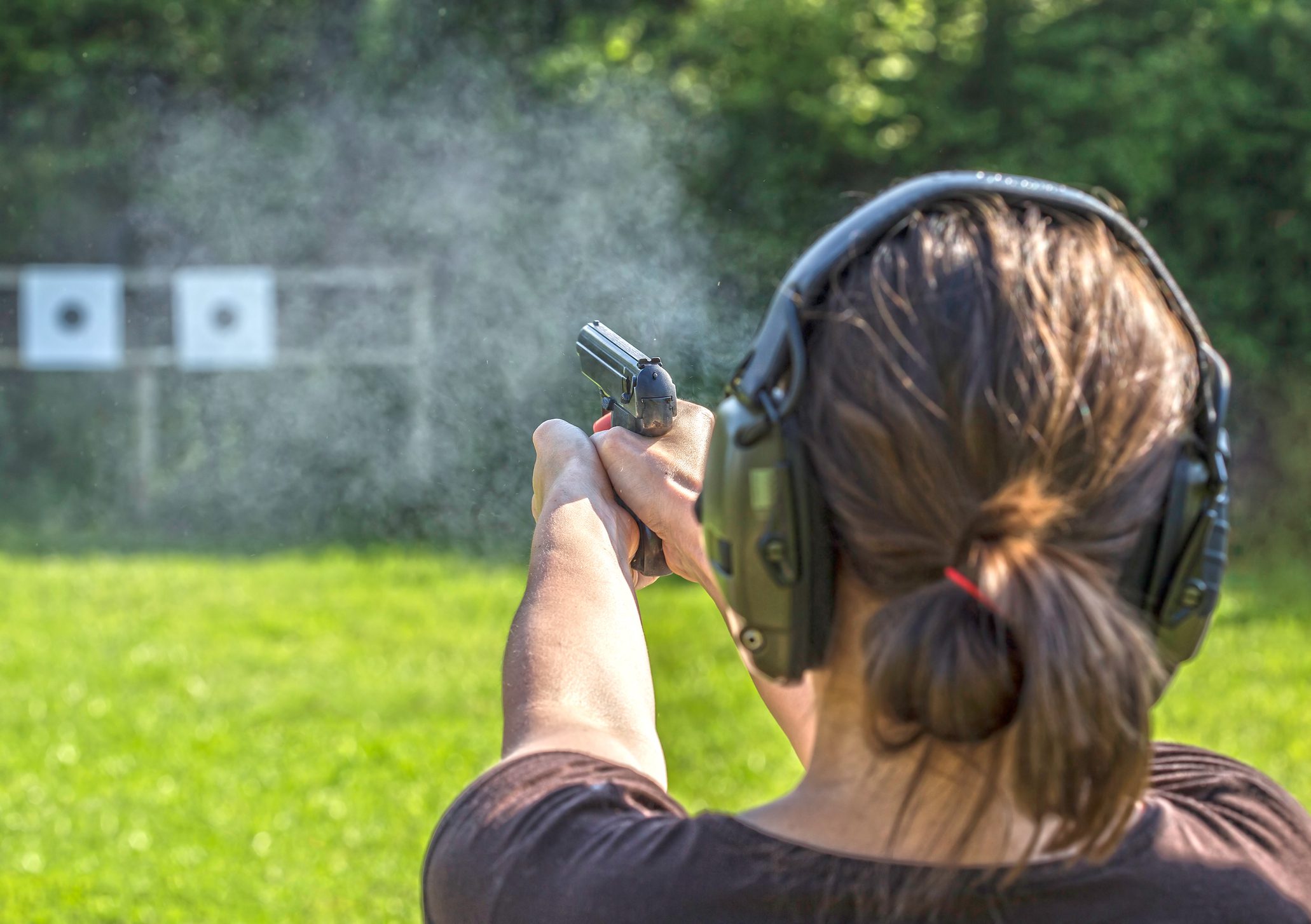 Woman wearing ear protection firing a gun at a target